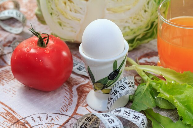 Bonito tomate rojo, huevo, repollo, ensalada, regla y jugo multivitamínico en vaso sobre la mesa