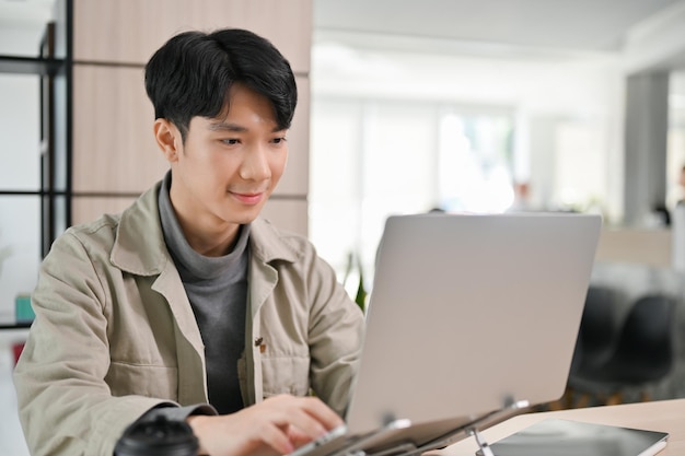 Bonito trabalhador de escritório asiático ou desenvolvedor trabalhando em sua tarefa no laptop no escritório