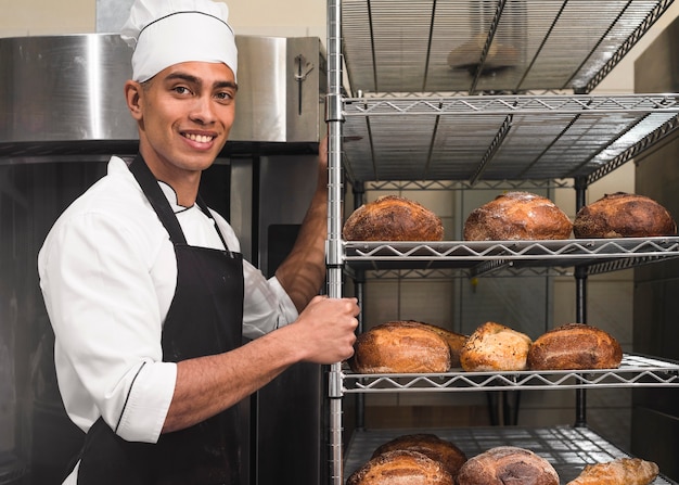 Bonito, trabalhador masculino, em, uniforme, carregar, prateleiras, com, loaf, de, pão, em, a, padaria