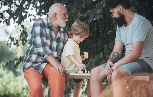 Bonito vovô e neto estão jogando xadrez enquanto passam tempo juntos menino ao ar livre com o pai