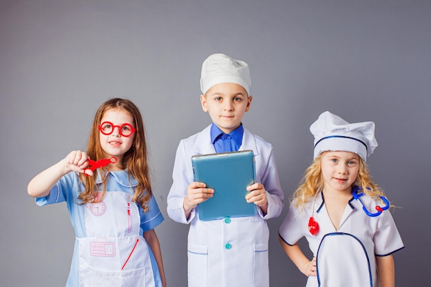 Bonitos filhinhos vestidos como médicos em fundo cinza