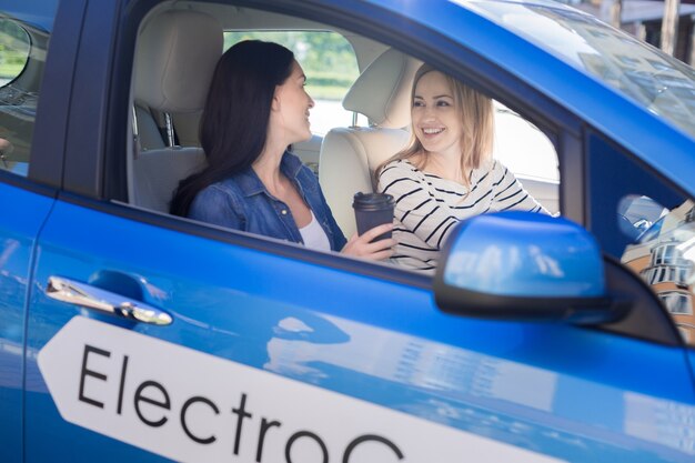 Bons amigos. Mulheres positivas e simpáticas encantadas tomando café e olhando uma para a outra enquanto andavam no carro elétrico