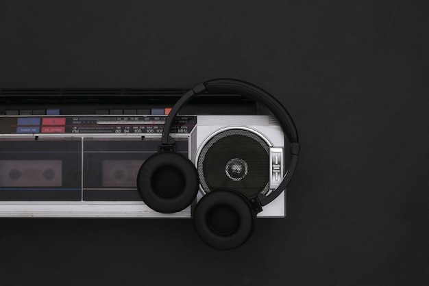 Foto boombox-tonbandgerät und stereo-kopfhörer auf schwarzem hintergrund. retro-80er jahre. ansicht von oben. flach legen