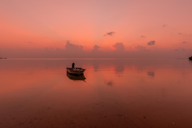 Foto boot, das in der abenddämmerung auf einem glatten rosa ozean schwimmt