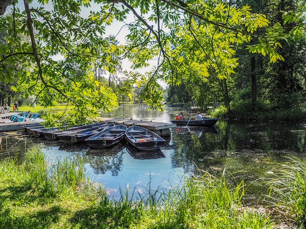 Boote auf dem Pier im Stadtpark. Sommerpark mit See. Angedocktes hölzernes Ruderboot.