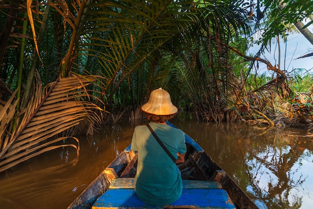 Bootstour in der Region Mekong-Delta, Ben Tre, Südvietnam. Tourist mit vietnamesischem Hut auf Kreuzfahrt in den Wasserkanälen durch KokosnussPalmeplantage.