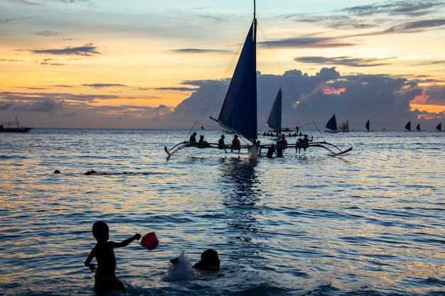 Boracay 18 SEP 2015 Philippinen Silhouetten eines Paares und eines Kindes im Meer und Segelboote bei Sonnenuntergang auf Boracay, einer tropischen Paradiesinsel auf den Philippinen