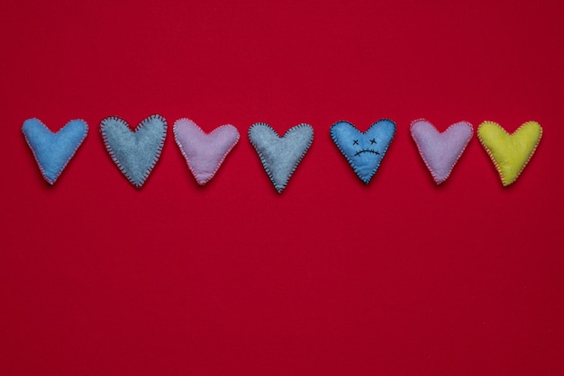 Foto bordado de corazón muerto triste entre corazones variables multicolores sobre una superficie de fieltro