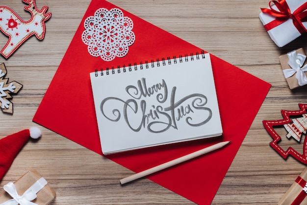 Borde de adornos de año nuevo y regalos sobre fondo de madera con deseos de Feliz Navidad escritos con fuente caligráfica