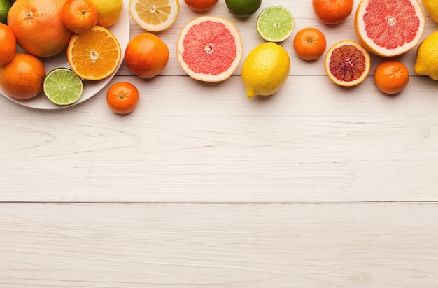 Borde de cítricos surtidos sobre fondo blanco de madera, espacio de copia. Vista superior de naranjas, limones, mandarinas y otras frutas exóticas, plano