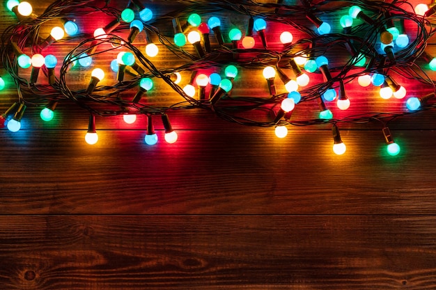 Foto borde de navidad con guirnalda de colores. fondo de navidad en el escritorio de madera oscura.