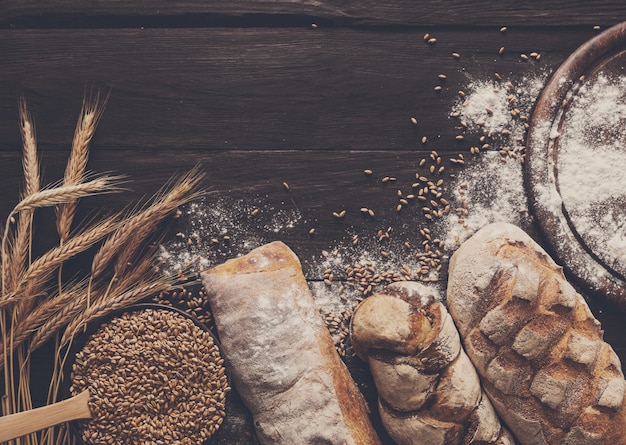 Borde de pan sobre fondo de madera. Composición de naturaleza muerta de panes de grano entero marrón y blanco con espigas de trigo esparcidas alrededor. Concepto de tienda de alimentos de panadería y abarrotes.