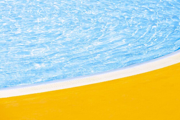 borde de la piscina al aire libre con borde curvo en un soleado día de verano agua azul clara y suelo amarillo.