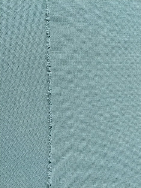 Borde rasgado de tela de lana fina en verde o azul Hilos sueltos en el borde de una pieza textil Primer plano Fondo tejido Color verde pastel tranquilo