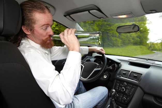 Borracho en coche con una botella de alcohol