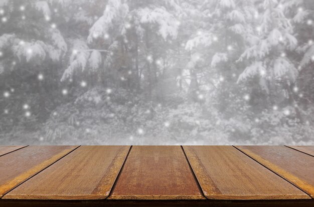 Borrosa nevando en el bosque de pinos a través del fondo de la ventana de vidrio con mesa de madera.