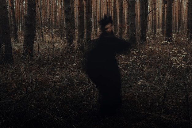 Foto borrosa silueta negra aterradora de una bruja malvada en un bosque oscuro