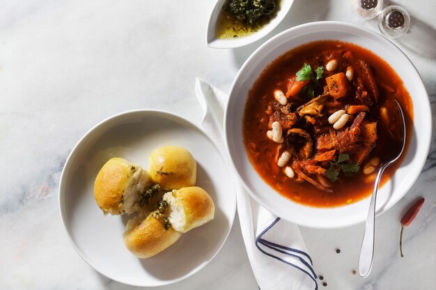 Borsch de sopa ucraniana con champiñones y frijoles blancos y panecillos pampushki en una mesa de mármol