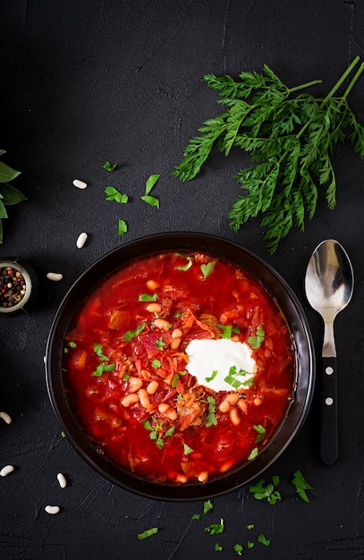 Borsch ucraniano tradicional do russo com feijões brancos na bacia preta e ingredientes para a borsch. Postura plana. Vista do topo.