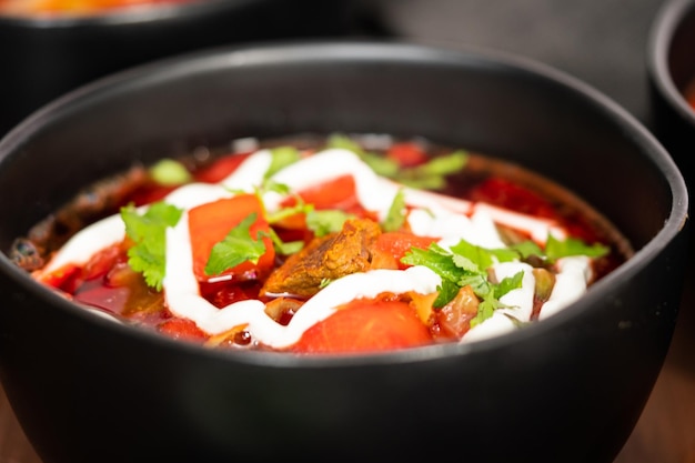 Borscht adornado con crema agria y perejil en un tazón negro.