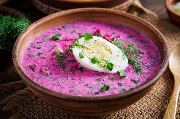 Borscht frío, sopa de remolacha de verano con pepino fresco, huevo cocido y patatas al horno en la mesa de madera. Comida tradicional europea, delicioso almuerzo.