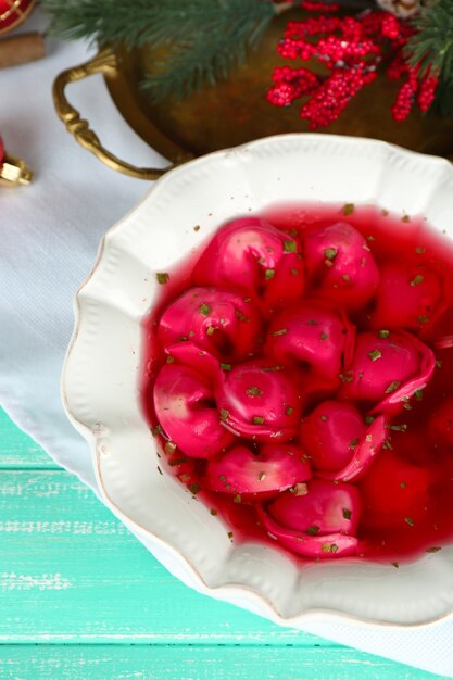 Borscht rojo claro polaco tradicional con bolas de masa y adornos navideños sobre fondo de mesa de madera de color