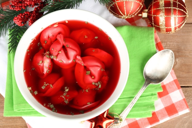 Borscht rojo claro polaco tradicional con bolas de masa y adornos navideños sobre fondo de mesa de madera