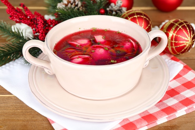 Borscht rojo claro polaco tradicional con bolas de masa y adornos navideños en la superficie de la mesa de madera