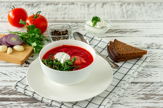 Borscht russo ucraniano tradicional com alho e pão. uma tigela de borscht de beterraba vermelha em uma mesa de madeira branca. sopa de beterraba. cozinha tradicional eslava.