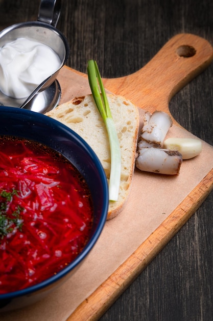 Borscht servido com creme azedo de banha de cebola e pão integral em um fundo de madeira