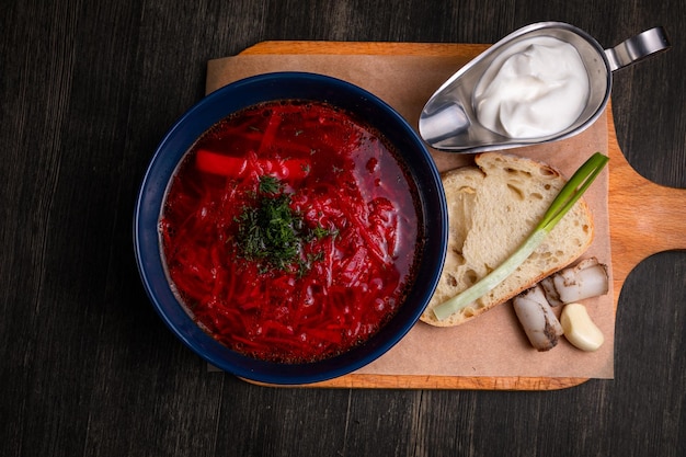 Borscht servido com creme azedo de banha de cebola e pão integral em um fundo de madeira