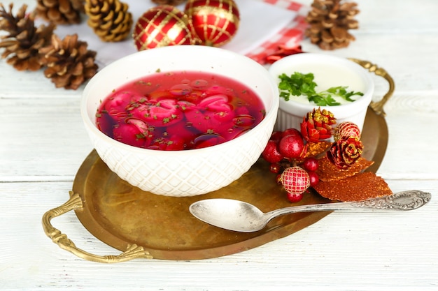 Borscht vermelho transparente polonês tradicional com bolinhos em uma tigela na bandeja e decorações de Natal na superfície de madeira