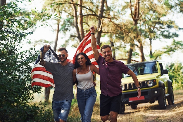 En el bosque. Los amigos tienen un buen fin de semana al aire libre cerca de su coche verde con la bandera de Estados Unidos.