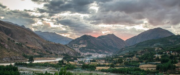 bosque cercano con río y montañas distantes, puesta de sol en cielo nublado, urcospampa, cusco, perú