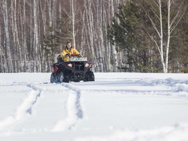 Un bosque de invierno una joven mujer sonriente con una chaqueta amarilla brillante montando una moto de nieve