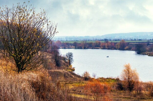 Bosque de otoño con árboles desnudos junto al río en tiempo nublado