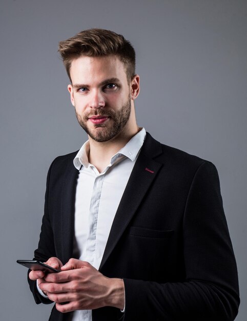 Boss männlich mit Handy sexy CEO auf grauem Hintergrund modernes Büroleben charismatischer Geschäftsinhaber stilvoller Makler gutaussehender Mann im Anzug selbstbewusster Geschäftsmann nutzt Smartphone