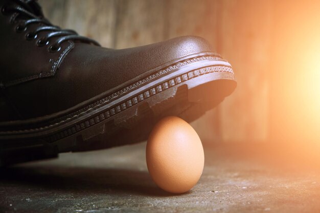 Bota negra y un frágil huevo de gallina con un brillo soleado. El concepto, el débil indefenso.