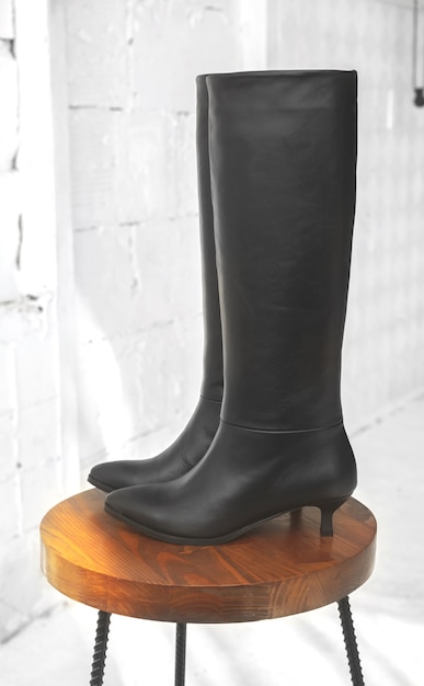 Foto botas de agua altas negras para mujer. calzado sobre soporte de madera. concepto de calzado femenino de otoño e invierno.