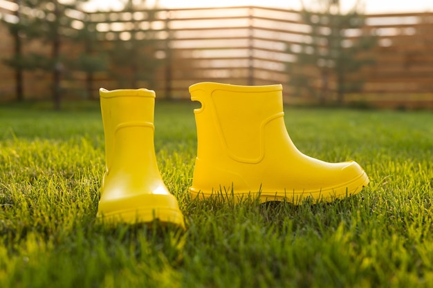 Botas amarelas ficam no gramado verde no jardim primavera verão e conceito de vida no campo