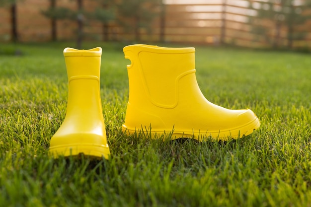 Botas amarelas ficam no gramado verde no jardim primavera verão e conceito de vida no campo