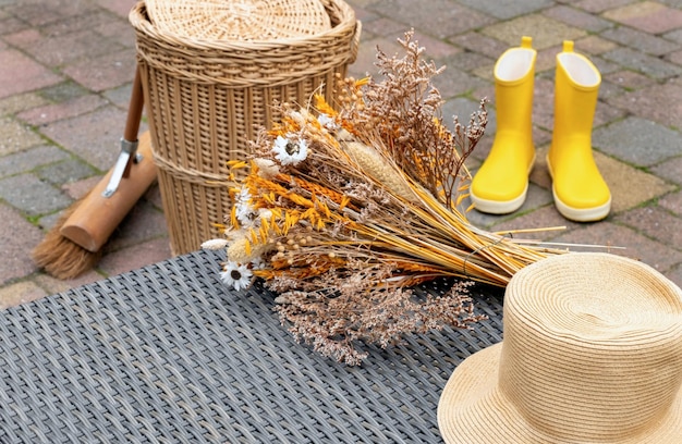 Foto botas amarelas flores secas cesta de vime com vassoura no jardim de outono