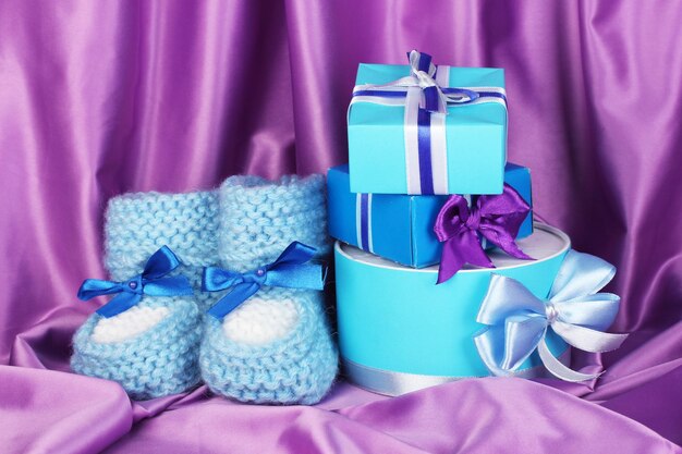 Botas de bebé azul y regalos sobre fondo de seda