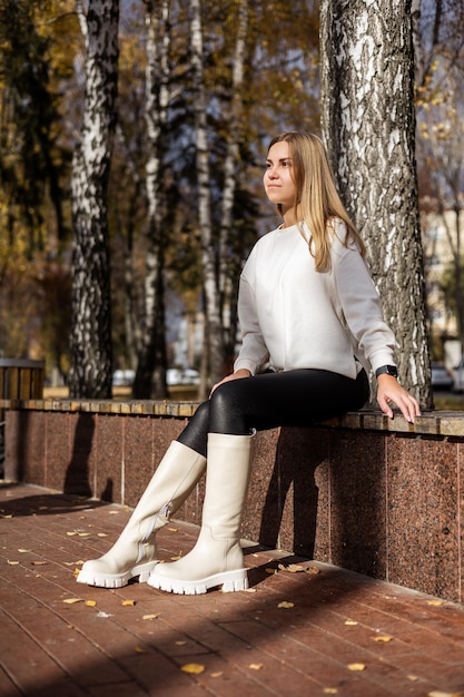 Botas blancas con cuero genuino en las piernas de una mujer joven. Mujer con ropa elegante y botas de trompeta blancas. Delgadas piernas delgadas con botas de invierno