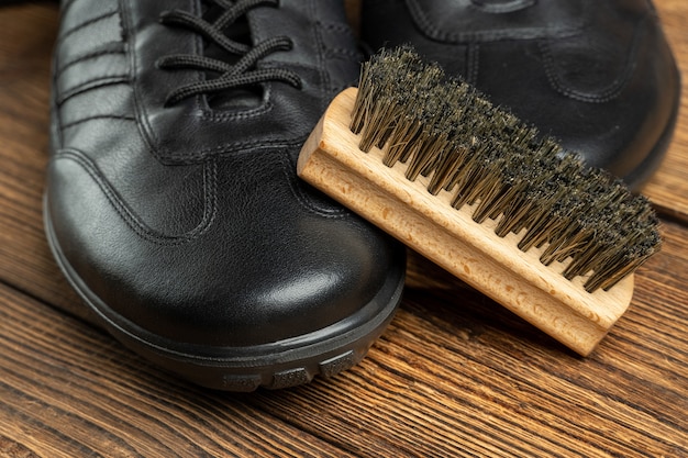 Foto botas de cuero, cepillo para lustrar zapatos, productos para el cuidado del calzado sobre fondo de madera