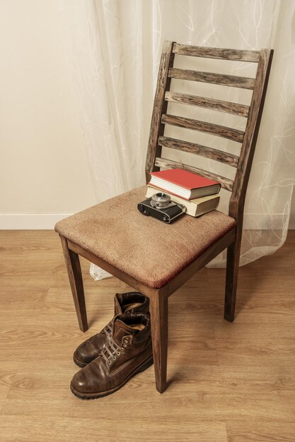 Foto botas de cuero marrón al lado de una cámara antigua y algunos libros en una vieja silla tapizada