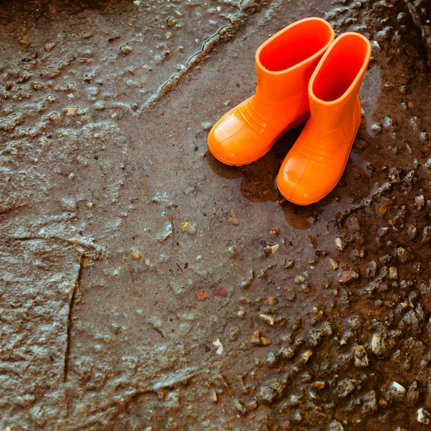 Foto botas de borracha laranja em pé ao lado da poça.