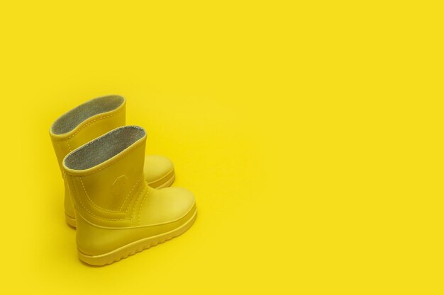 Botas de borracha para crianças amarelas em um fundo amarelo com espaço de cópia