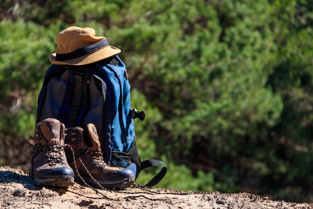 Botas de caminhada de mochila turística e chapéu na clareira na floresta de pinheiros