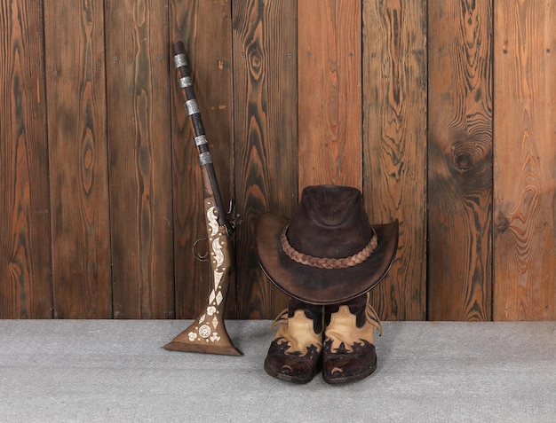 Foto botas de chapéu de cowboy e arma em um chão de madeira